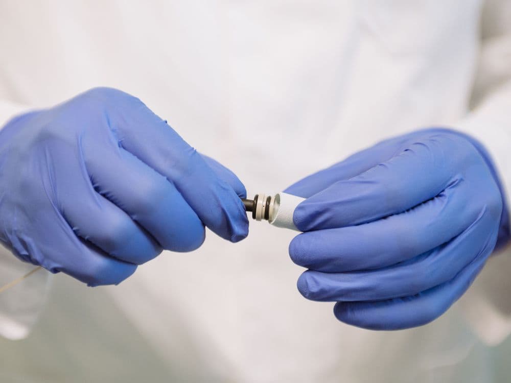 Hands in blue gloves carefully examine a small technical component with precision.