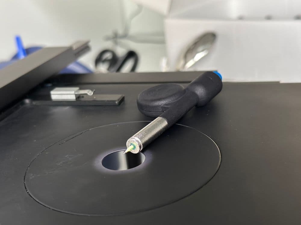 Precision probe with metallic tip on a black circular scientific instrument platform.