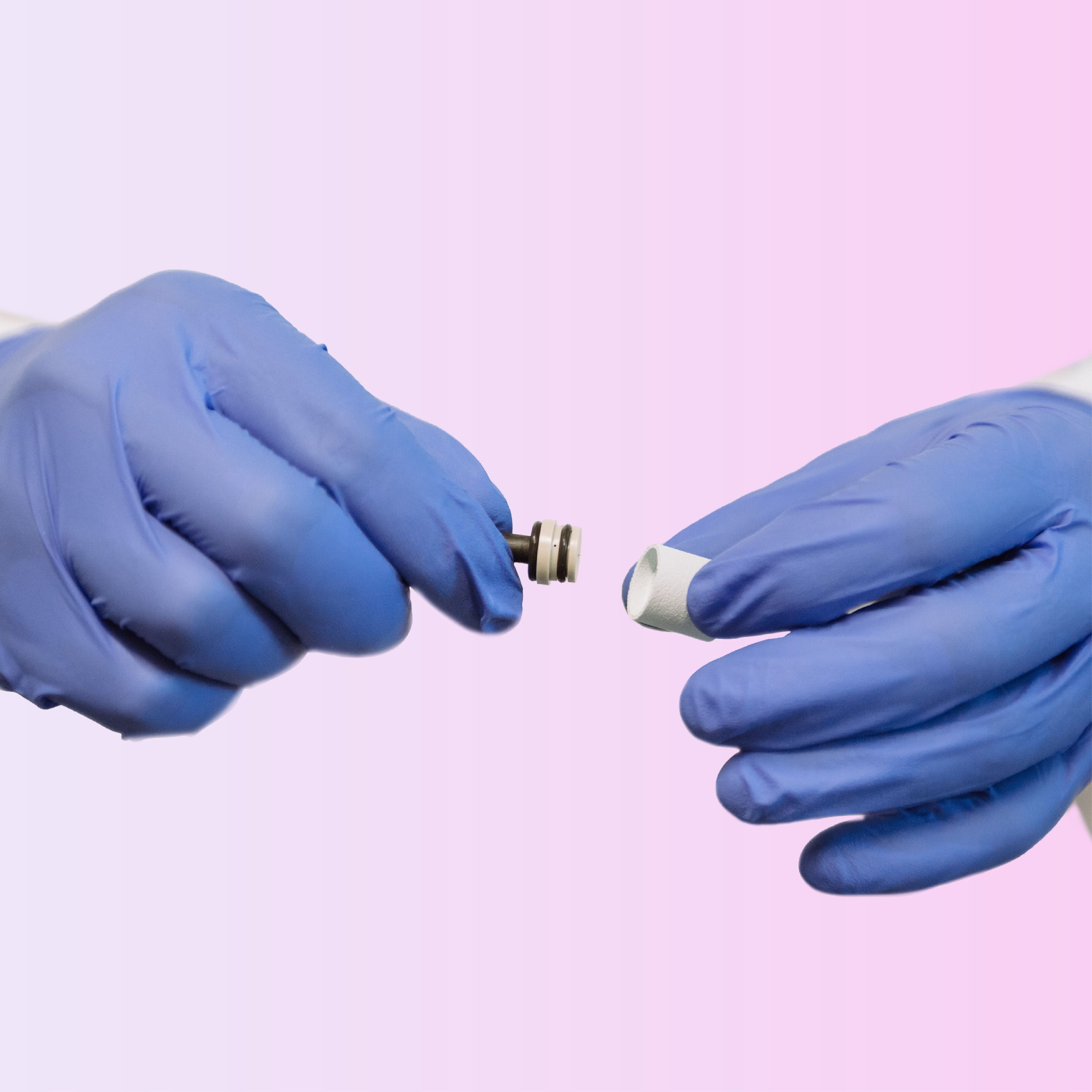 Hands in blue gloves holding small metallic and white cylindrical components.